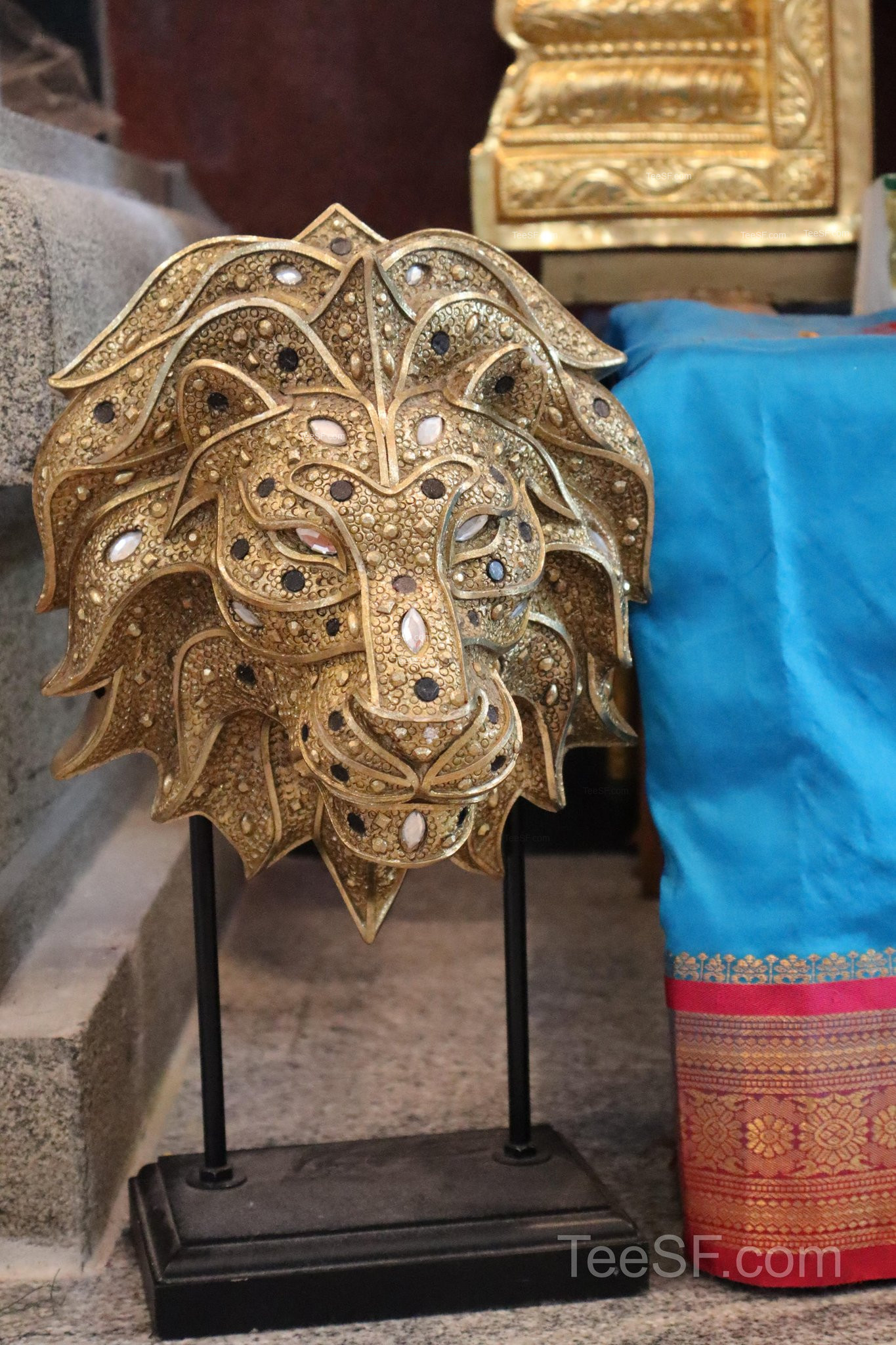 A close view of a detailed gold temple ornament beside colorful fabric.